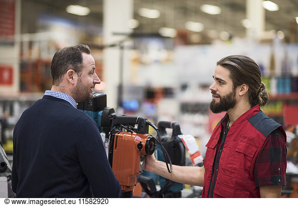 Salesman discussing over machinery with male customer in hardware store
