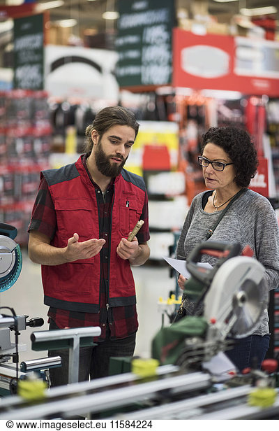 Salesman explaining power tools to mature woman in hardware store
