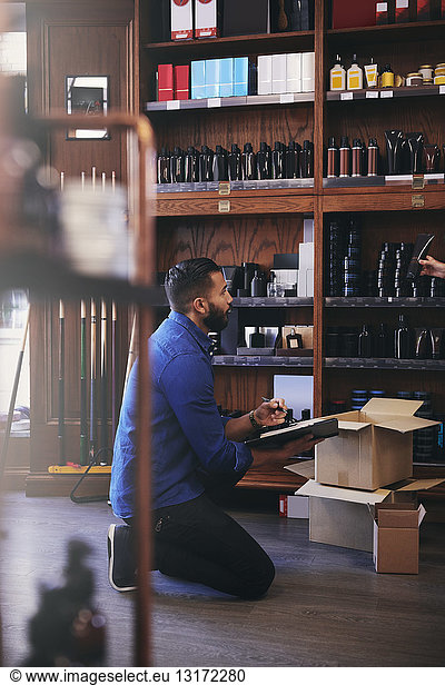 Salesman kneeling while looking at beauty product being held by colleague in deli
