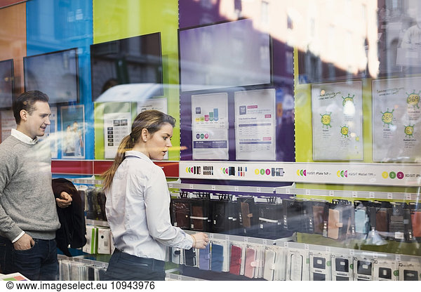 Saleswoman assisting man in buying phone cover seen through glass