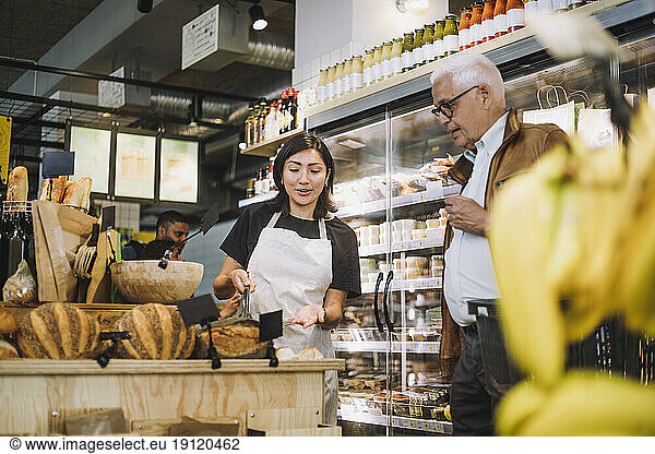Saleswoman discussing over bread with senior male customer in grocery store