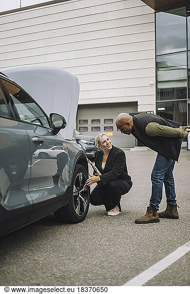 Saleswoman explaining about wheel to male customer while crouching near car