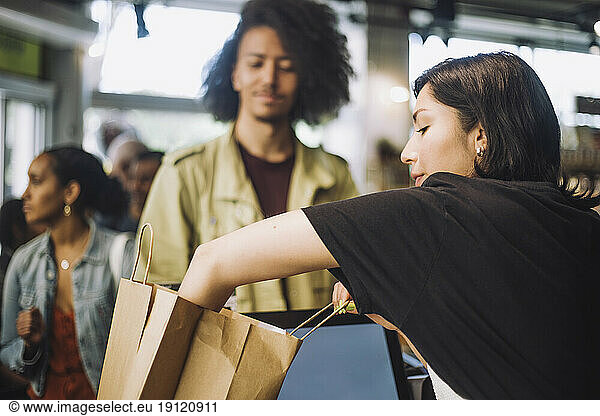 Saleswoman packing bag while customer standing at grocery store checkout