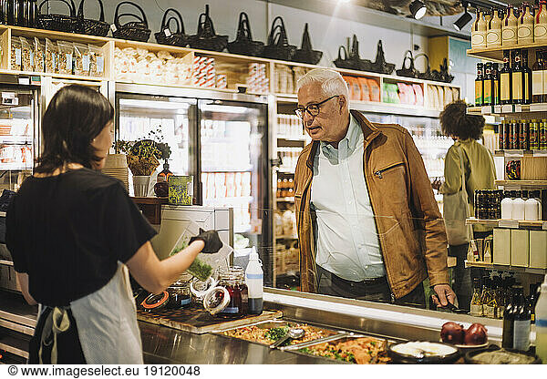 Saleswoman showing container to senior male customer at delicatessen