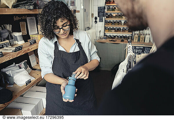 Saleswoman showing reusable bottle to male customer at organic store