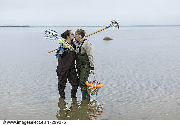 Same sex female couple in waders kissing and standing in ocean