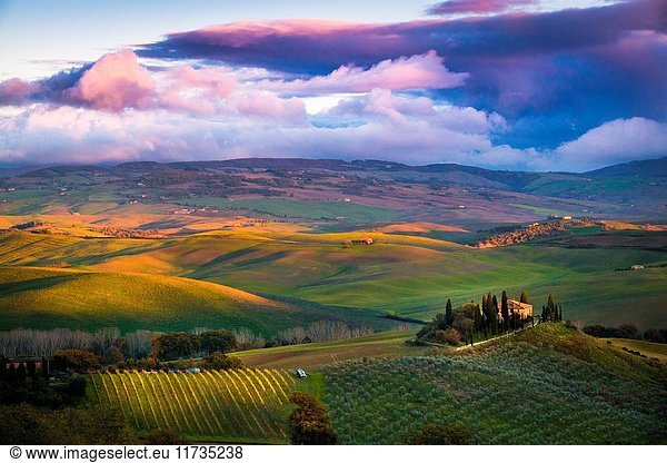 San Quirico d'Orcia  Tuscany  Italy. Sunset over the valley with some farmhouses and a very cloudy sky.