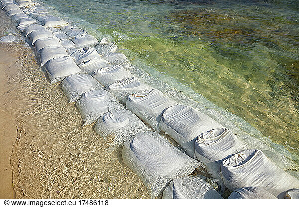 Sandsäcke in Reihen an der Wasserkante  um die Erosion des Strandes zu verhindern