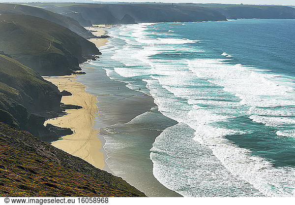 Sandy beaches with surf along a grassy cliff shoreline with blue sky and clouds; Cornwall County  England