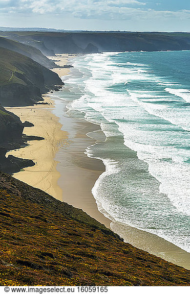 Sandy beaches with surf along a grassy cliff shoreline with blue sky and clouds; Cornwall County  England