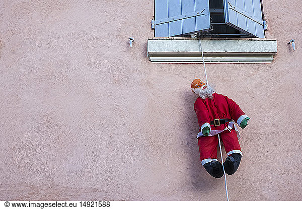 Santa Claus figure hanging on rope from a window of house with pink facade.