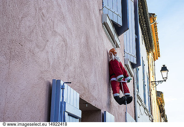 Santa Claus figure hanging on rope from a window of house with pink facade.