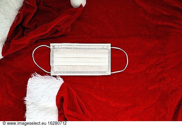 Santa Claus rote Mütze mit medizinischen Gesichtsmaske auf Santa Claus Anzug Stoff  Covid-19 und Weihnachten Konzept  Hintergrund Textur Schönheit.