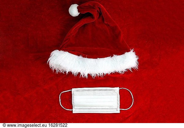 Santa Claus rote Mütze mit medizinischen Gesichtsmaske auf Santa Claus Anzug Stoff  Covid-19 und Weihnachten Konzept  Hintergrund Textur Schönheit.