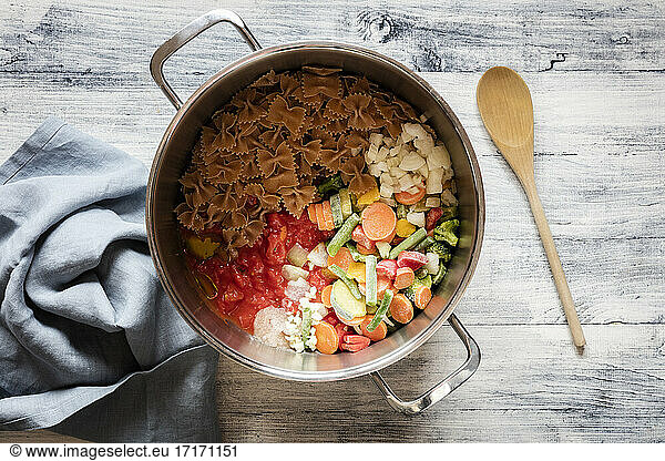 Saucepan with raw ingredients for vegan pasta with vegetables