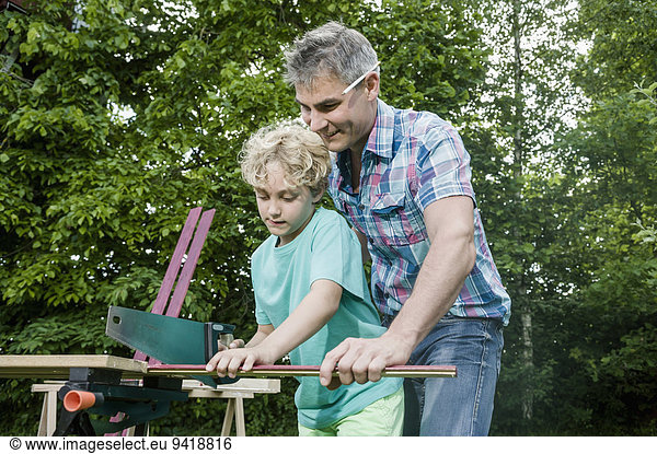 Sawing wood garden father son together