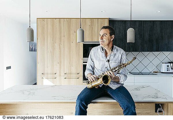 Saxophonist with saxophone sitting on kitchen island at home