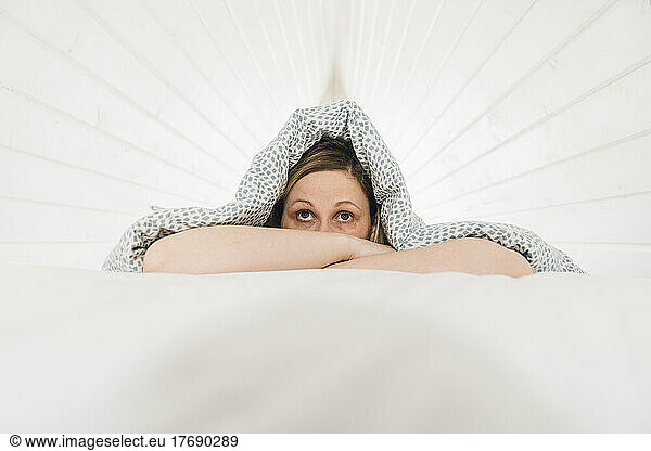 Scared woman lying under blanket on bed in attic