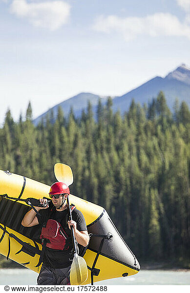 Scenic image of man carrying yellow raft (packraft) in wilderness.