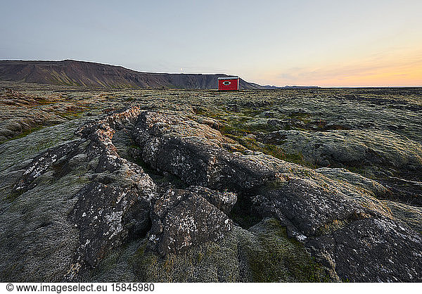 Scenic landscape of rocky location with cabin at sunset