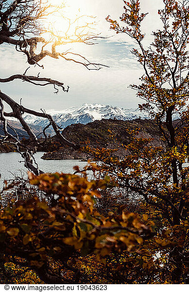 Scenic view of a lake and snowy mountains with a sun flare in autumn