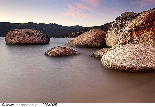 Scenic view of boulder rocks in sea during sunset