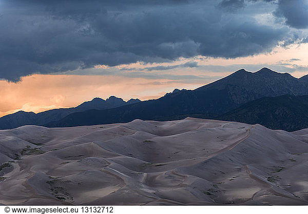 Scenic view of desert against mountains and stormy clouds at Great Sand Dunes National Park
