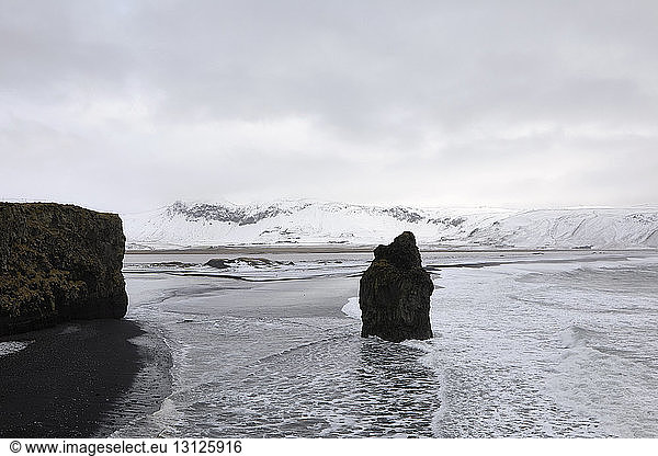 Scenic view of Dyrholaey Iceland and Arnardrangur rocks against cloudy sky during winter
