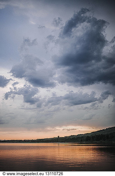 Scenic view of river against stormy clouds during sunset