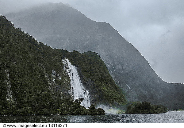 Scenic view of waterfalls against mountains at Milford sound during foggy weather