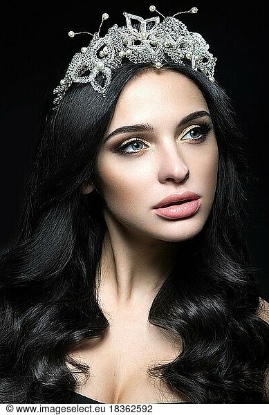 Schöne dunkelhaarige Frau mit einer Krone aus Edelsteinen  Locken und Abend-Make-up. Schönes Gesicht. Bild im Studio auf einem schwarzen Hintergrund aufgenommen