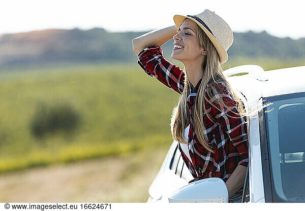 Schöne Frau mit Hut  die sich lächelnd aus dem Autofenster lehnt
