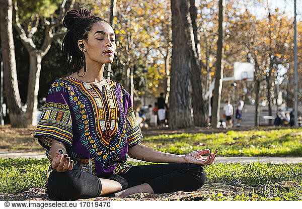 Schöne junge Frau meditiert  während sie Yoga im Lotussitz im Park an einem sonnigen Tag praktiziert