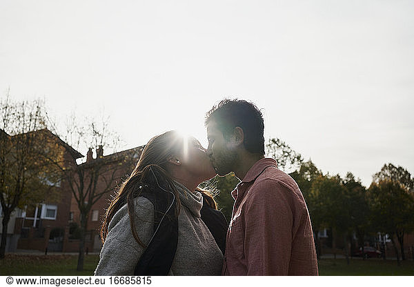 Schönes junges Paar  das sich bei Sonnenuntergang in einem Park küsst. Romantisches Konzept