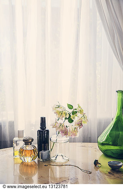 Schönheitsprodukte mit Schmuck durch Blumenvase auf Tisch gegen Vorhang