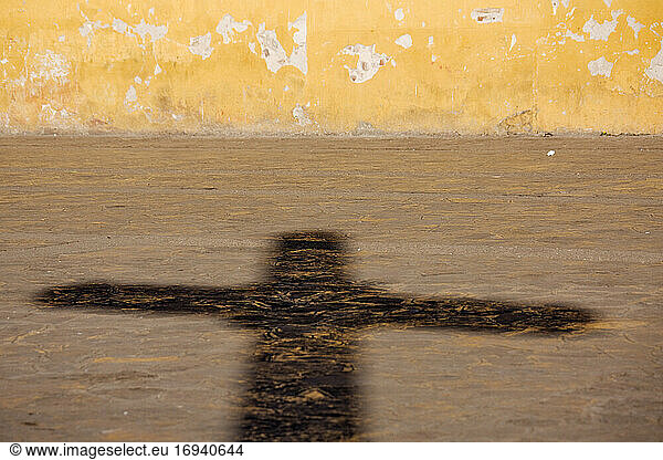 Schatten eines Kruzifixes auf einem Straßenpflaster.