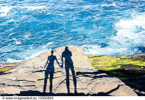 Schatten eines Mannes und einer Frau  die sich am Meer an Felsen festhalten
