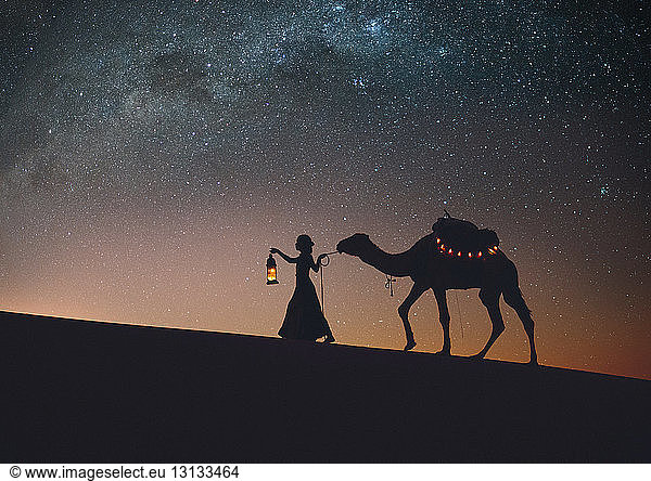 Scherenschnittfrau mit Kamel beim Spaziergang in der Wüste Sahara gegen Sternenfeld