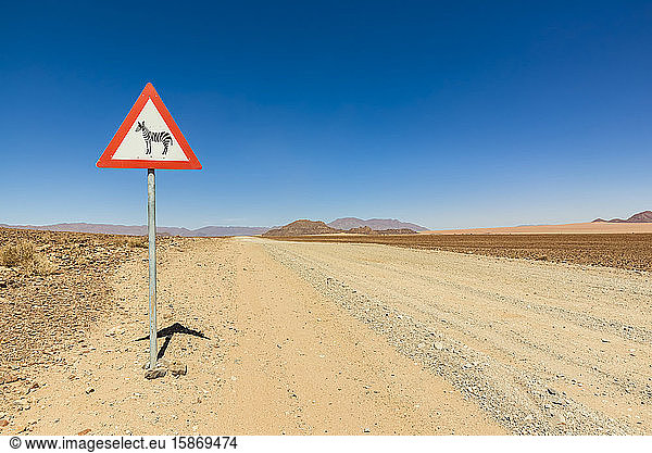 Schild Achtung Wildtiere an einer langen trockenen Straße  Namib-Wüste  Namib-Naukluft-Nationalpark; Namibia