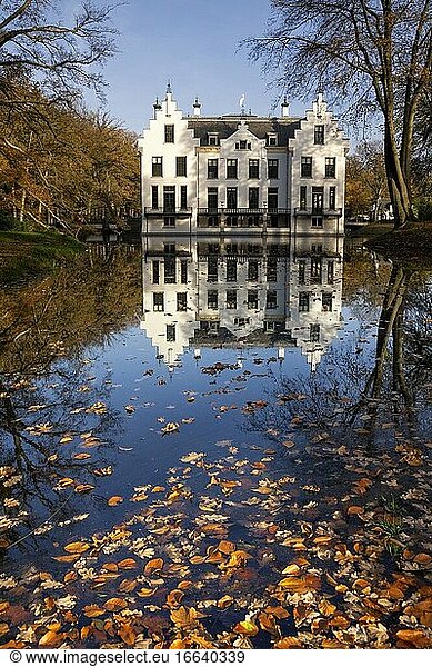 Schloss Staverden im niederländischen Naturgebiet Veluwe spiegelt sich im Wassergraben und ist von herbstlich gefärbten Bäumen umgeben.