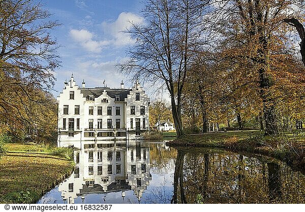 Schloss Staverden spiegelt sich im Wassergraben und ist von herbstlich gefärbten Bäumen umgeben.