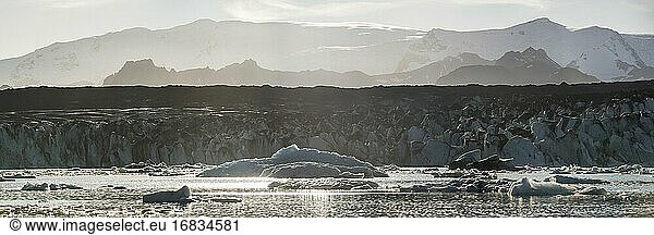 Schmelzende Gletscher und Eiskappen aufgrund des Klimawandels und der globalen Erwärmung  mit Eisbergen in der Lagune Jokulsarlon bei Sonnenuntergang  dahinter der Breidamerkurjokull-Gletscher  Südostisland