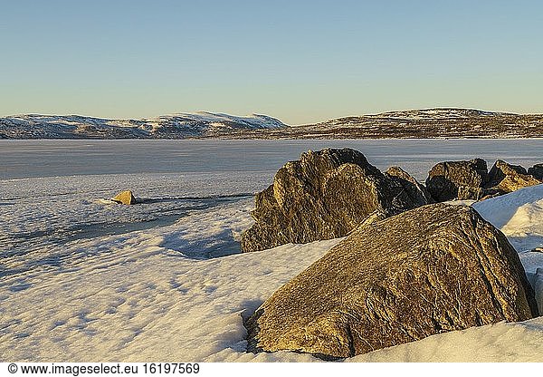 Schneelandschaft im Frühling mit Bergen im Hintergrund  zugefrorener See Tornetr?sk  große Felsen im Vordergrund  Bezirk Kiruna  Schwedisch-Lappland  Schweden.