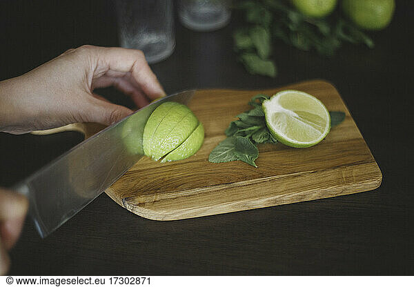 Schnitt der Hand  Messer und geschnittene Limette auf dem Holzbrett