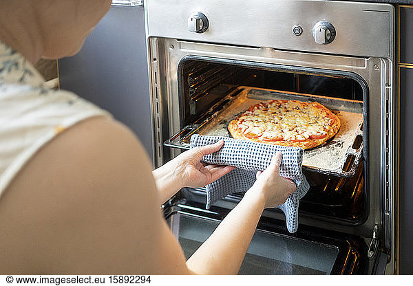 Schnittansicht einer Frau  die ein Tablett mit gebackener Pizza aus dem Ofen nimmt