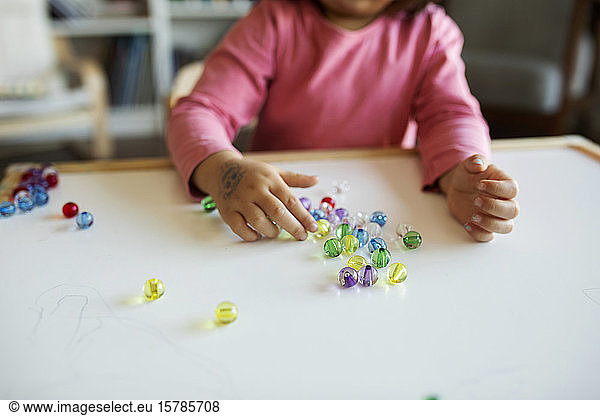 Schnittansicht eines Mädchens  das mit Murmeln auf dem Tisch spielt
