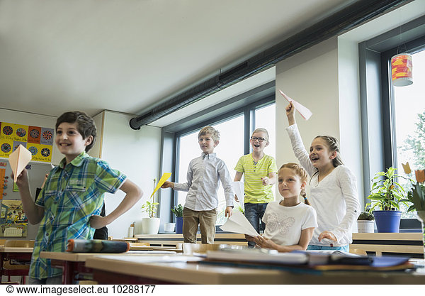 School children playing with paper airplanes in classroom  Munich  Bavaria  Germany