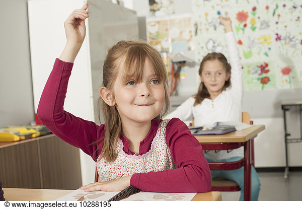 School children with raised hands in classroom  Munich  Bavaria  Germany