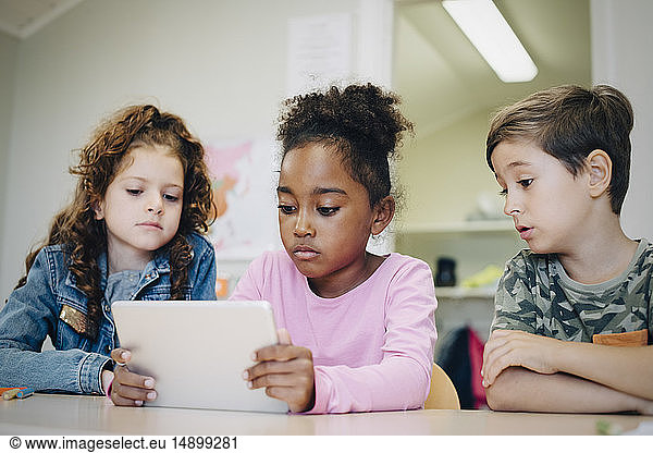 School friends learning through digital tablet at desk in classroom