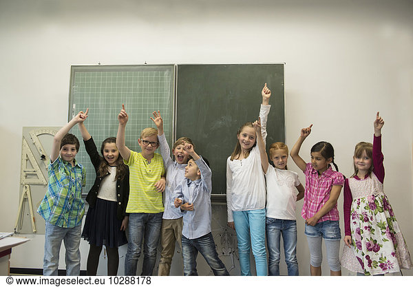 School students raising hands in front of blackboard in classroom  Munich  Bavaria  Germany